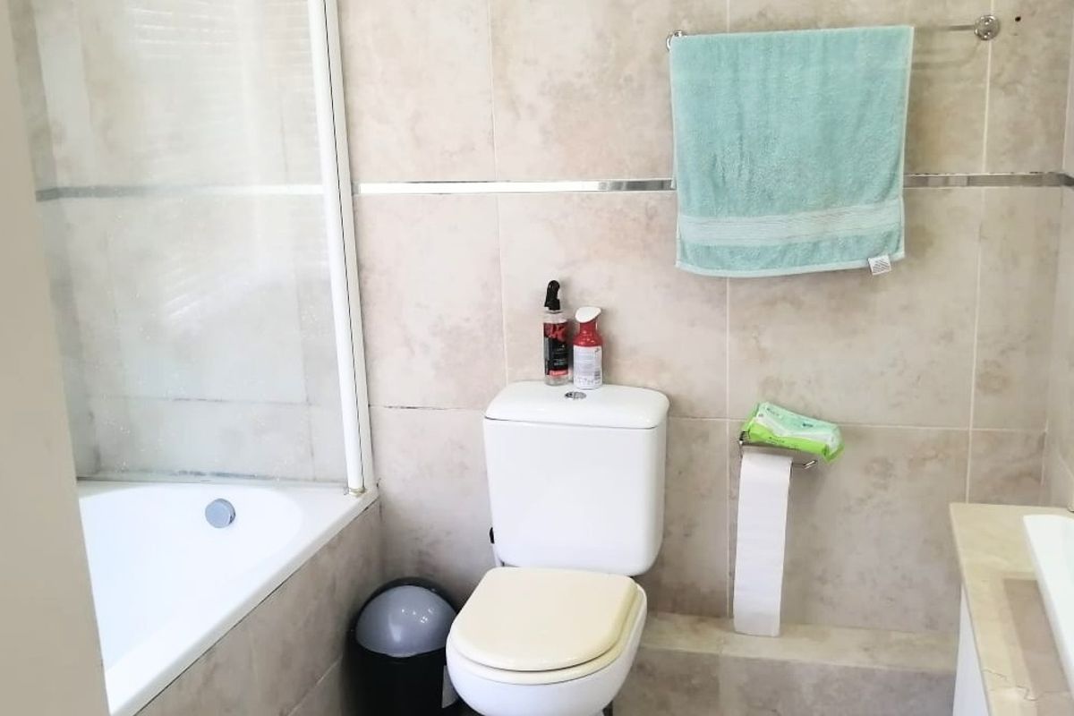 A functional bathroom featuring tiled walls, a bathtub with a glass shower screen, and a standard toilet.