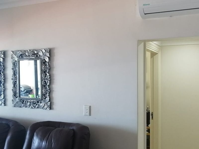 A view of a living room wall featuring a wall-mounted air conditioning unit and neutral wall finishes.