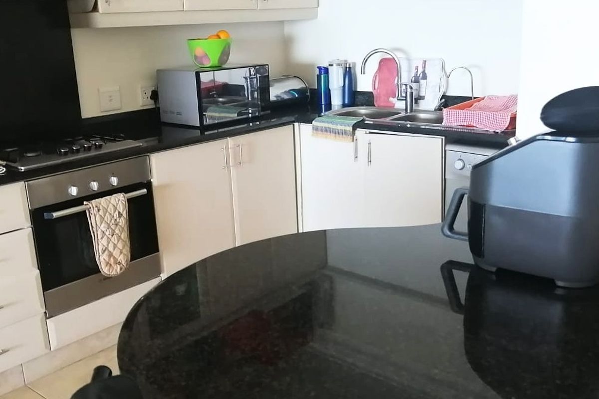 A functional kitchen featuring granite countertops, built-in oven, gas hob, and ample cabinetry with a double basin sink.