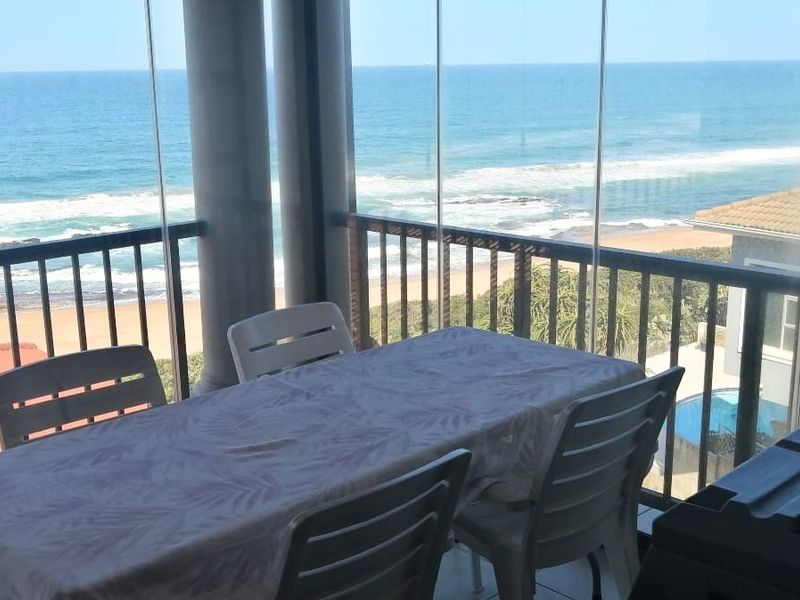 A covered balcony featuring a glass enclosure, offering expansive ocean views and a tiled floor, perfect for outdoor dining.