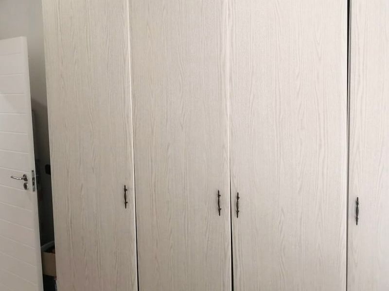A bedroom featuring light wood-grain built-in wardrobes and a white internal door, providing ample storage space.