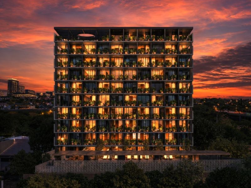 A striking modern apartment building facade at sunset, featuring integrated balcony greenery and extensive glass windows across multiple levels.