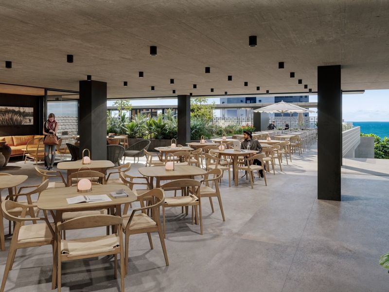 Modern open-plan clubhouse area featuring exposed concrete ceilings, recessed lighting, and seamless transition to an outdoor terrace with ocean views.
