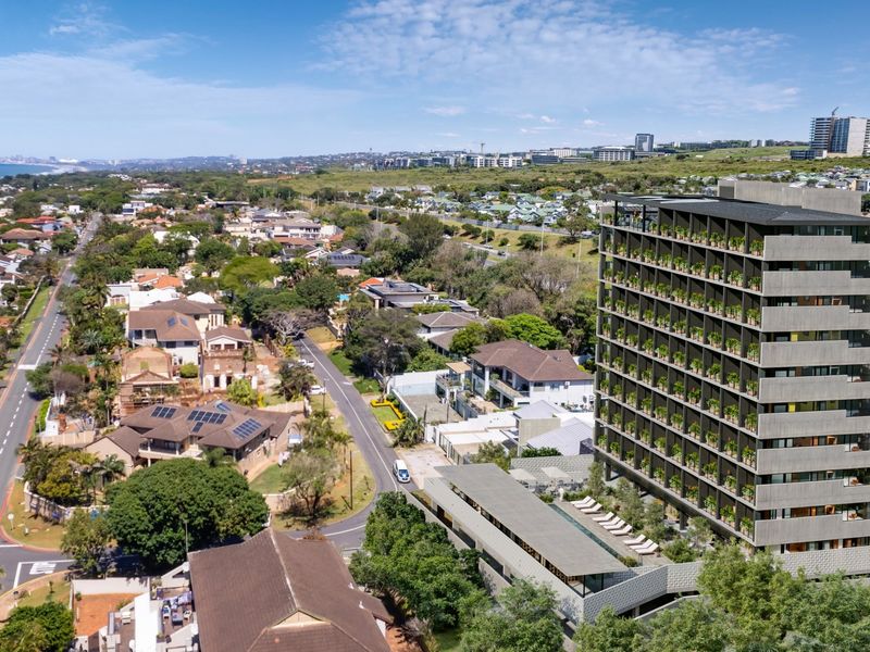Aerial view of a modern multi-story apartment complex featuring a swimming pool and landscaped surroundings in a coastal neighborhood setting.