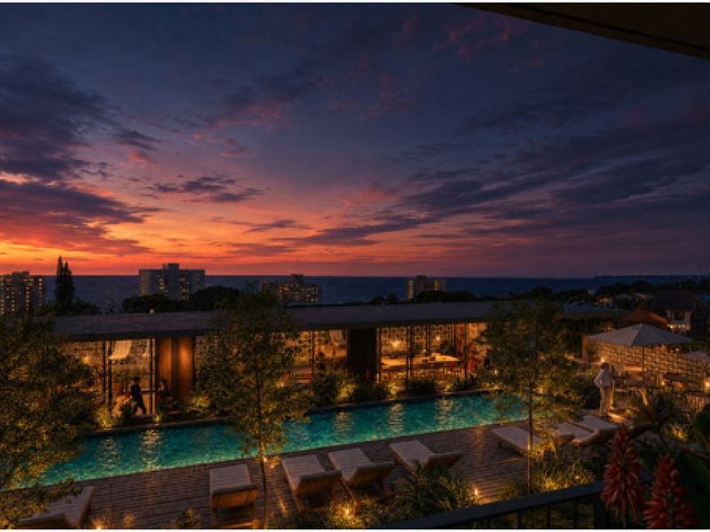 A beautifully lit outdoor pool area at sunset, featuring modern decking, lush landscaping, and a stunning coastal view.