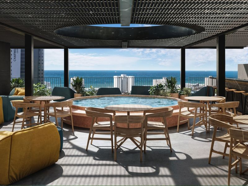 A modern rooftop pool area featuring a circular plunge pool, built-in bar, and a slatted pergola with panoramic ocean views.