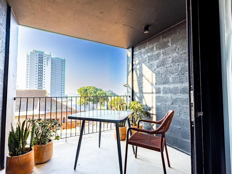 A modern covered balcony featuring exposed concrete block walls, a sleek metal railing, and a concrete floor with an urban city view.