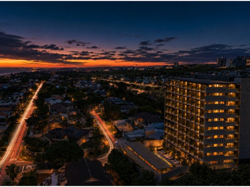 Stunning aerial twilight view of a modern multi-story apartment complex featuring a swimming pool and surrounding urban landscape.