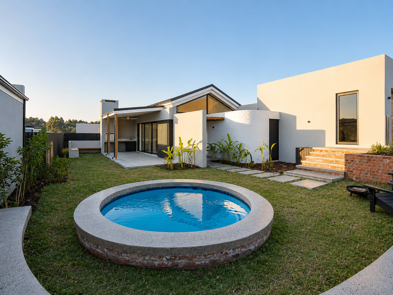 Modern rear exterior featuring a circular plunge pool, landscaped garden, covered patio with built-in braai, and contemporary architectural design.