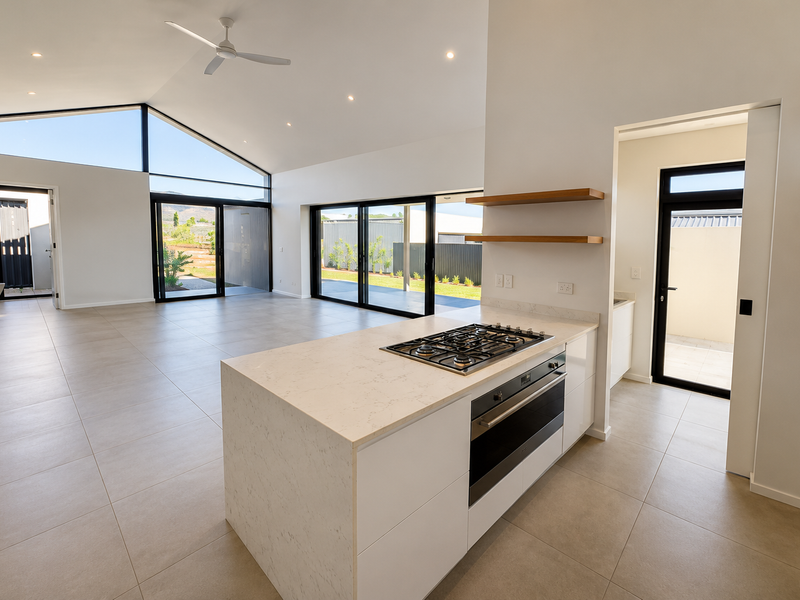 Spacious open-plan living and kitchen area featuring a modern island with gas cooktop, raked ceilings, and large sliding doors opening to the exterior.