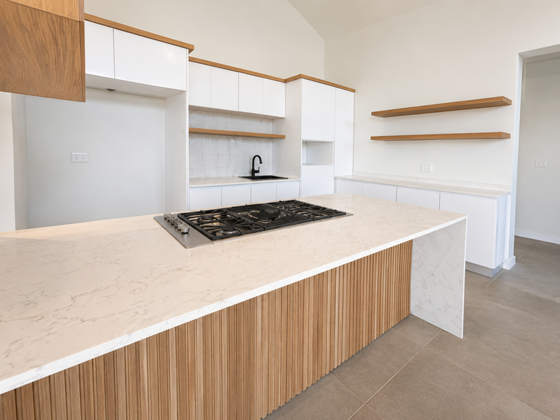 Modern kitchen featuring a large island with a gas cooktop, quartz countertops, sleek white and timber cabinetry, and floating shelves.