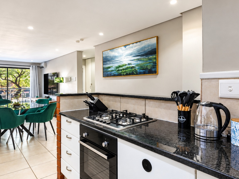 Modern open-plan kitchen and dining area featuring granite countertops, gas hob, built-in oven, and tiled flooring with access to a balcony.