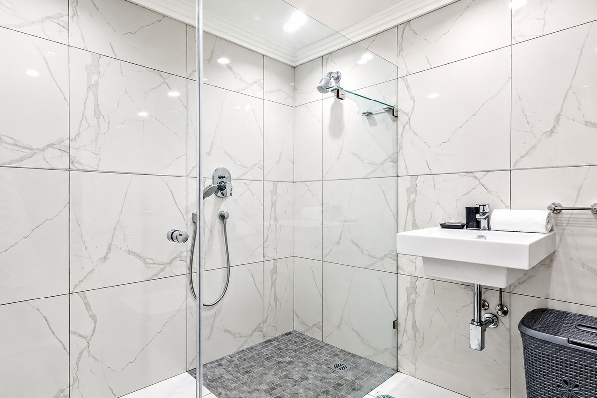 Modern bathroom featuring a walk-in shower with glass screen, marble-effect wall tiling, mosaic floor tiles, and a sleek wall-mounted basin.