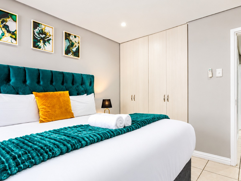 A well-maintained bedroom featuring built-in cupboards, neutral tiled flooring, and recessed downlighting, with a clean, modern aesthetic.