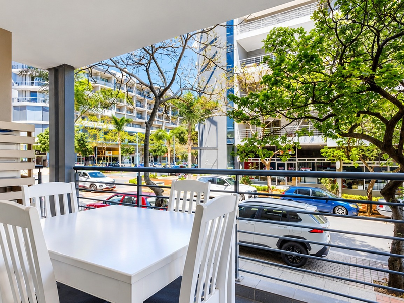 A covered balcony featuring tiled flooring, a metal balustrade, and an integrated air conditioning unit, overlooking a street-level urban environment.