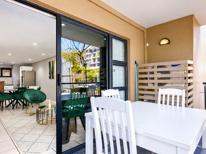 A covered balcony featuring tiled flooring, a sliding glass door entrance, and a wall-mounted air conditioning unit, providing a seamless transition to the interior living space.