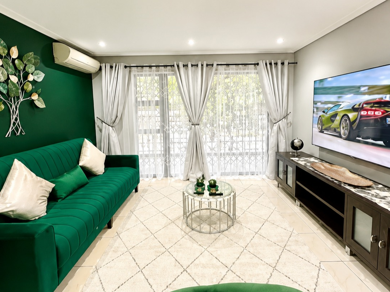 A well-maintained living room featuring tiled flooring, recessed downlighting, and a split-system air conditioner, with direct access to an outdoor area via sliding doors.