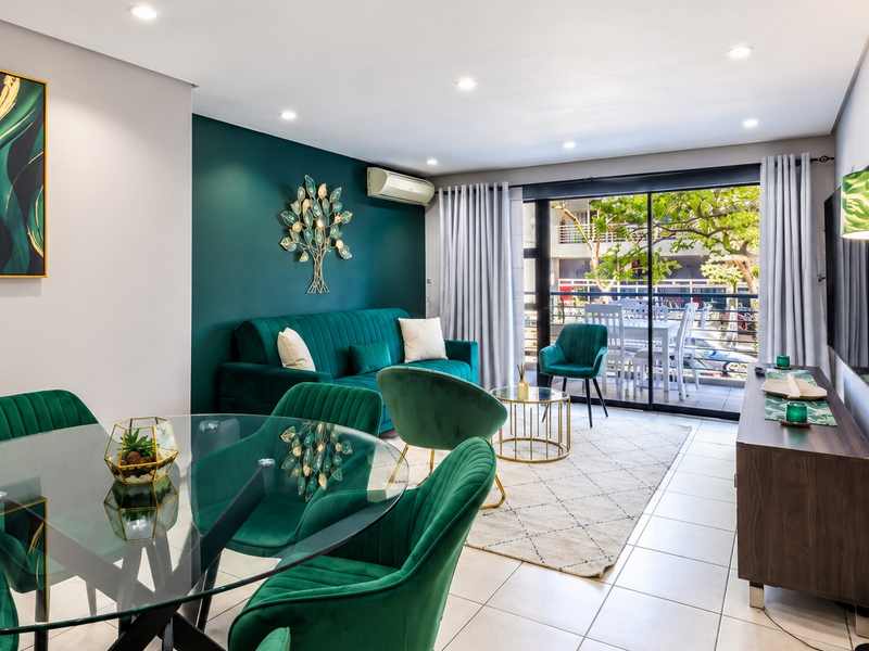 A bright open-plan living and dining area featuring tiled floors, recessed lighting, a split-system air conditioner, and large sliding doors leading to a balcony.