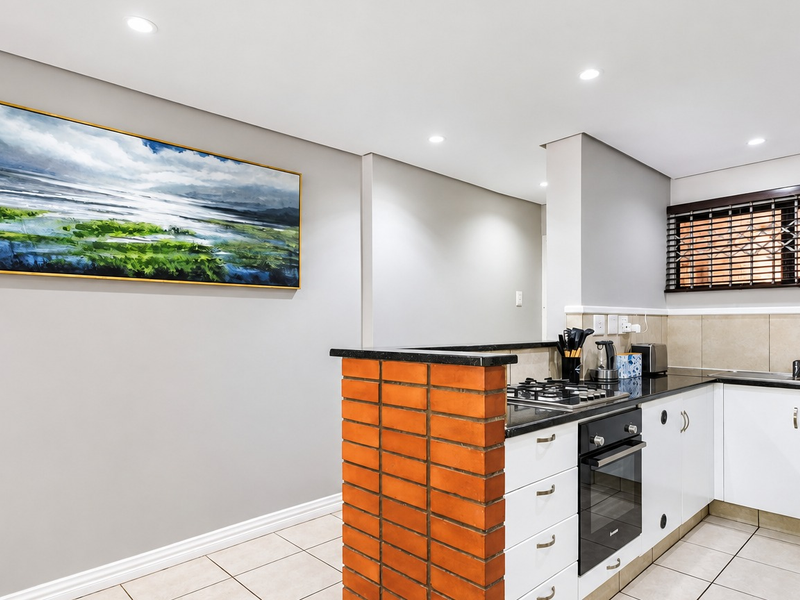 Modern kitchen featuring white cabinetry, granite countertops, built-in oven, gas hob, and tiled flooring with recessed lighting.