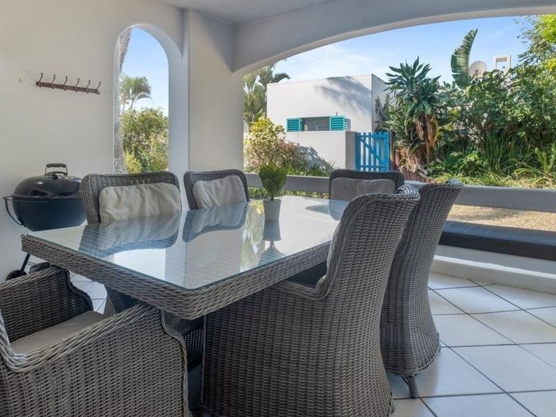 A covered patio area featuring tiled flooring, a built-in bench, and an arched opening overlooking the garden.