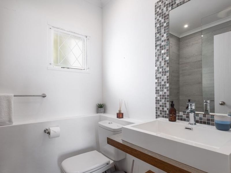 A modern bathroom featuring a sleek vanity basin with mosaic tile detailing, a large wall-mounted mirror, and a toilet.