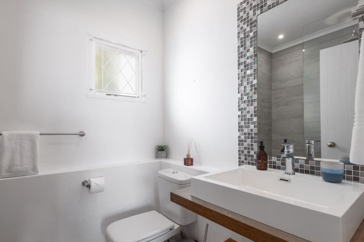 A modern bathroom featuring a sleek vanity basin with mosaic tile detailing, a large wall-mounted mirror, and a toilet.