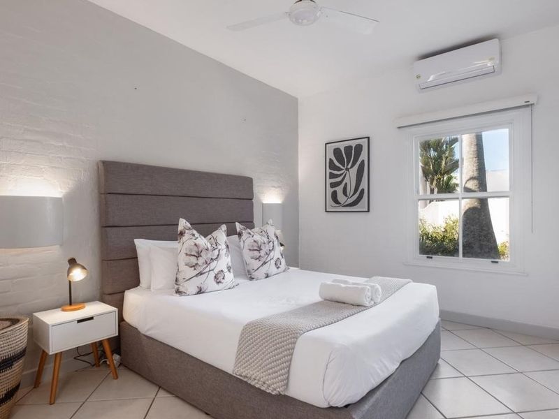 A bright and well-maintained bedroom featuring tiled flooring, a painted brick feature wall, a ceiling fan, and a split-system air conditioner.