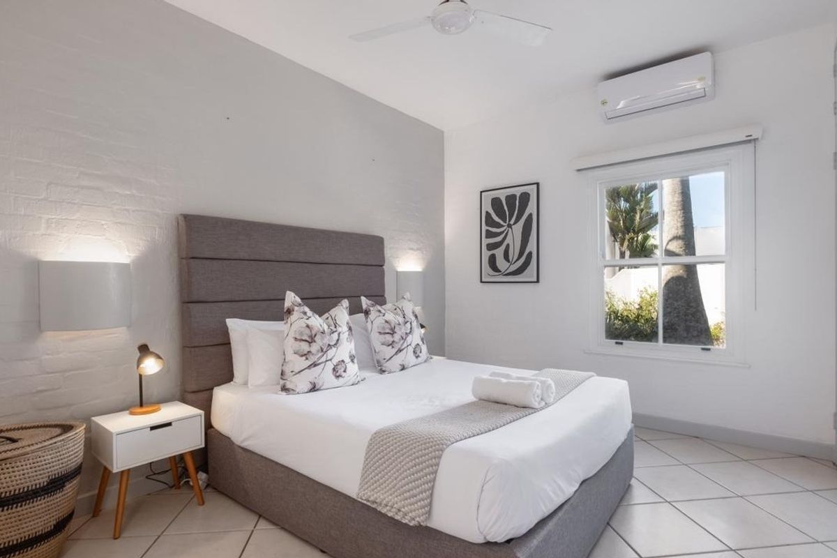 A bright and well-maintained bedroom featuring tiled flooring, a painted brick feature wall, a ceiling fan, and a split-system air conditioner.