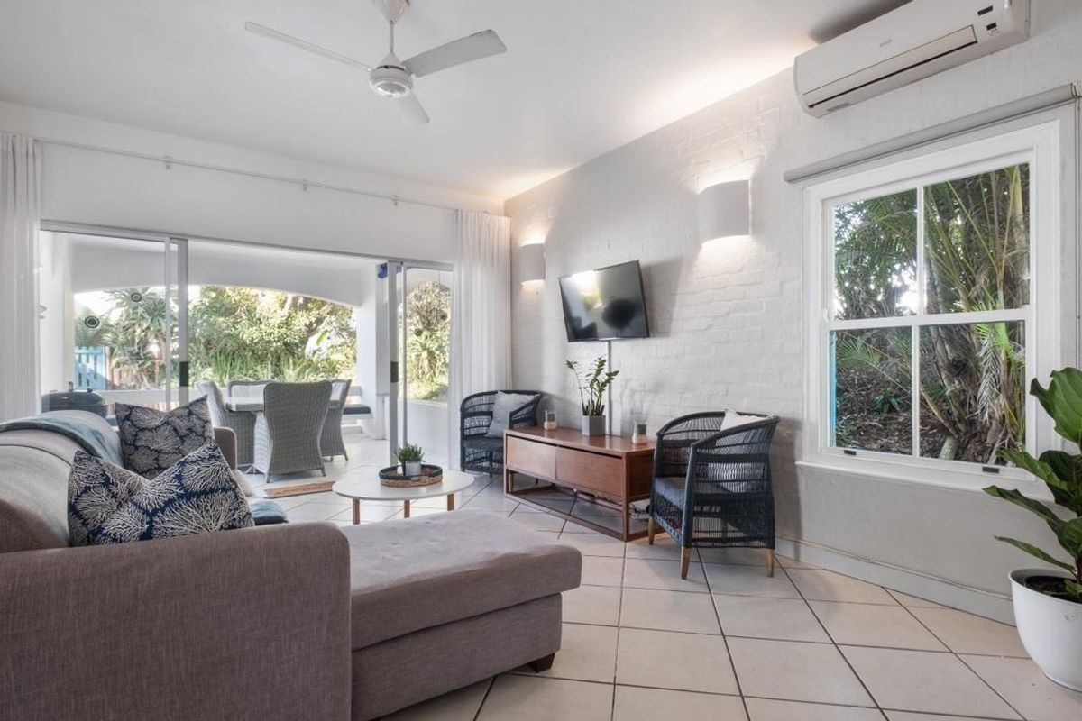 Bright and airy living room featuring tiled floors, a split-system air conditioner, ceiling fan, and large sliding doors opening to an outdoor patio area.
