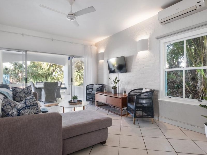 Bright and airy living room featuring tiled floors, a split-system air conditioner, ceiling fan, and large sliding doors opening to an outdoor patio area.