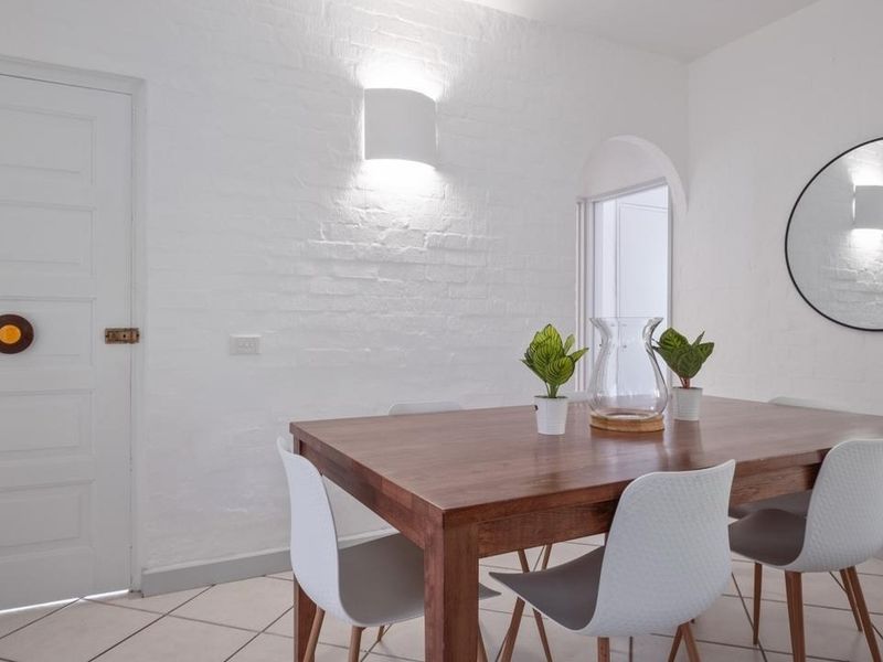 A bright dining area featuring painted brick walls, tiled flooring, and an arched doorway, creating a clean and modern aesthetic.