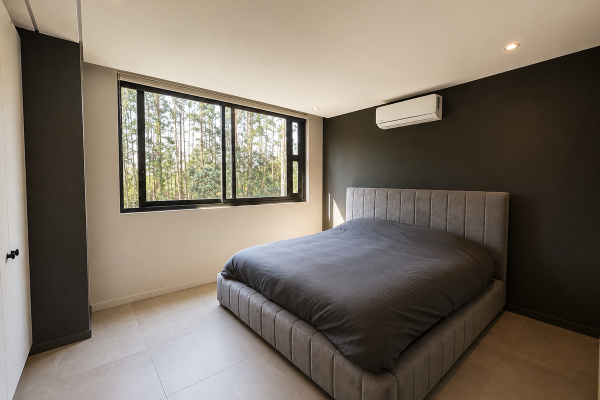 Modern bedroom featuring neutral tiled flooring, dark accent walls, a split-system air conditioner, and large sliding windows with a natural forest view.