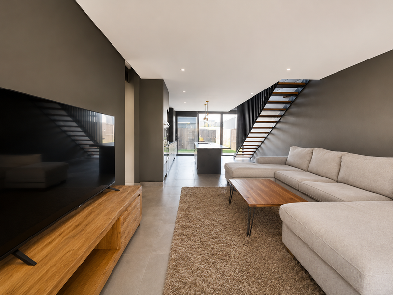 Modern open-plan living area featuring a sleek kitchen, tiled floors, and a contemporary staircase leading to the upper level with access to the rear.