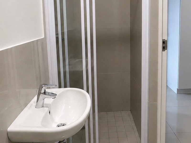 A clean and modern bathroom featuring a wall-mounted basin with a chrome mixer tap and a separate shower enclosure with tiled finishes.