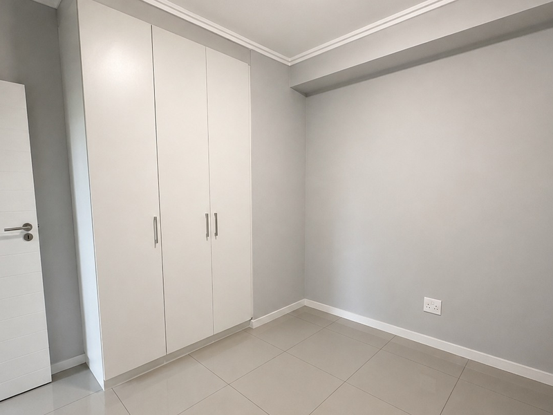 A clean, empty bedroom featuring neutral grey walls, modern tiled flooring, and white built-in cupboards with sleek hardware.