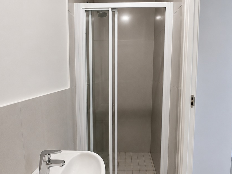 A clean, modern bathroom featuring a tiled shower enclosure with a glass door and a contemporary basin with a mixer tap.