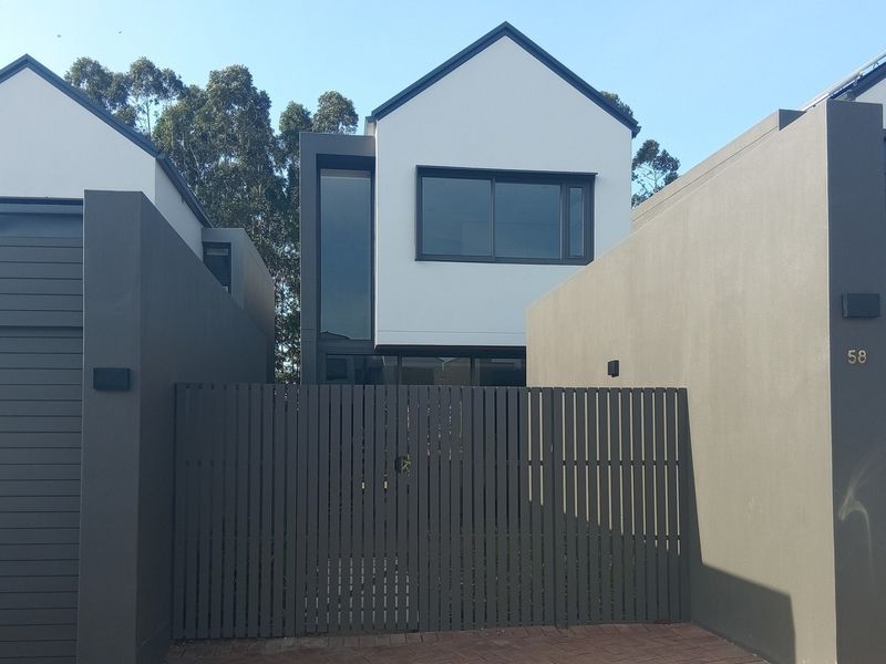Modern townhouse exterior featuring a clean white facade, dark grey accents, and a secure slatted gate entrance.