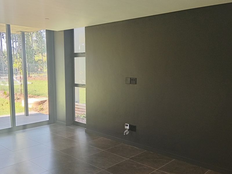 A modern, empty living area featuring large format floor tiles, dark feature wall, and expansive aluminium sliding doors providing direct access to the garden.