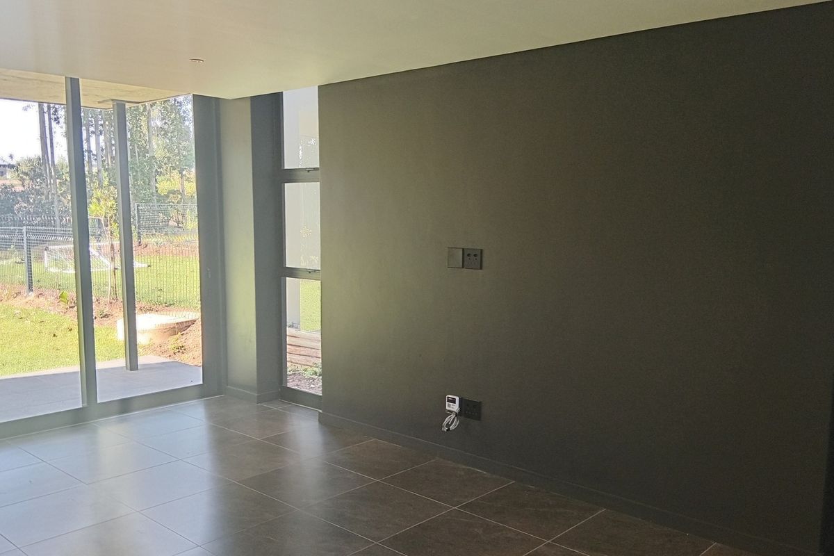 A modern, empty living area featuring large format floor tiles, dark feature wall, and expansive aluminium sliding doors providing direct access to the garden.