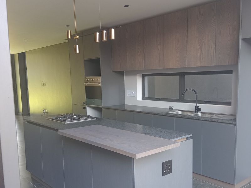 Modern kitchen featuring sleek grey cabinetry, stone countertops, a central island with a gas hob, and integrated built-in appliances.