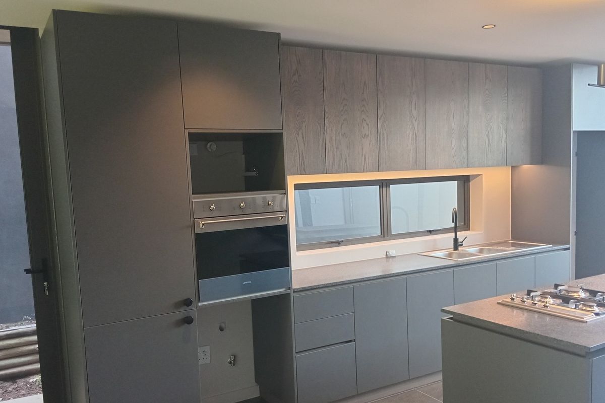 Modern kitchen featuring sleek grey cabinetry, a central island with a gas hob, built-in oven, and integrated stainless steel sink with contemporary finishes.