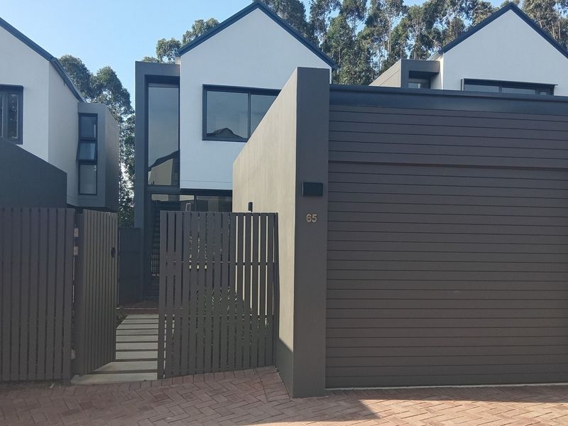 Modern townhouse exterior featuring a sleek garage door, timber slat fencing, and a paved pedestrian entrance with a stone pathway.