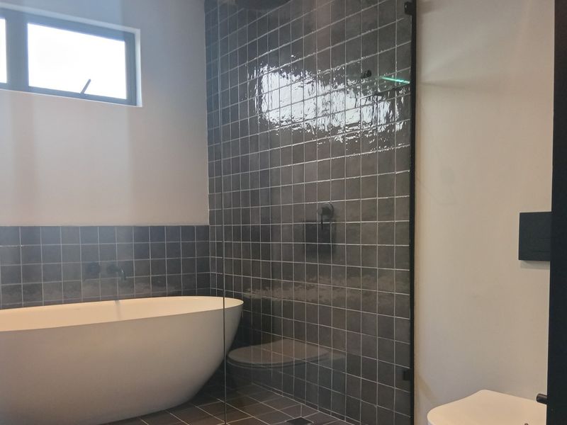 Modern bathroom featuring a sleek freestanding bathtub, a spacious walk-in shower with dark tiled walls, and contemporary fixtures.