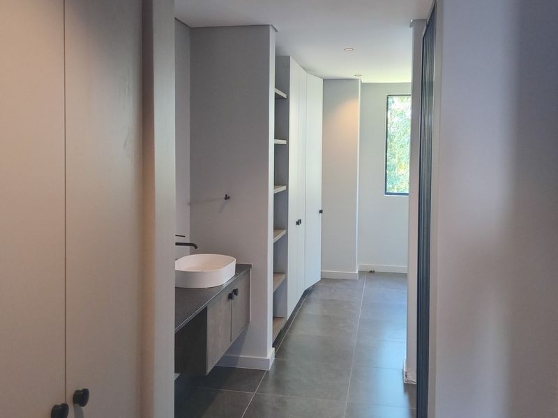 A modern, minimalist bathroom featuring a floating vanity with a vessel sink, built-in cabinetry, and sleek tiled flooring in a neutral color palette.
