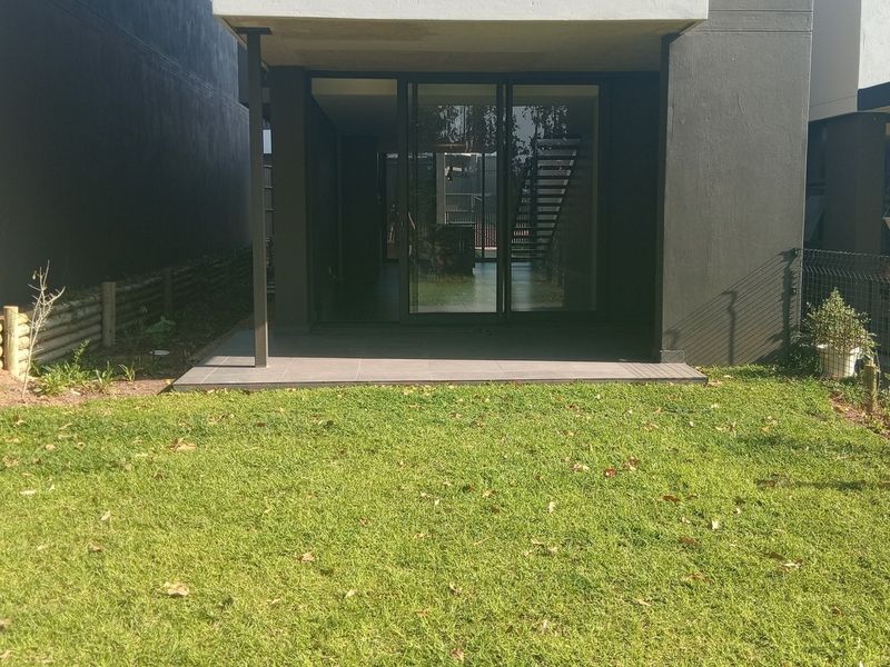 Rear view of the townhouse featuring a private lawn, a tiled patio area, and large sliding glass doors providing access to the interior.