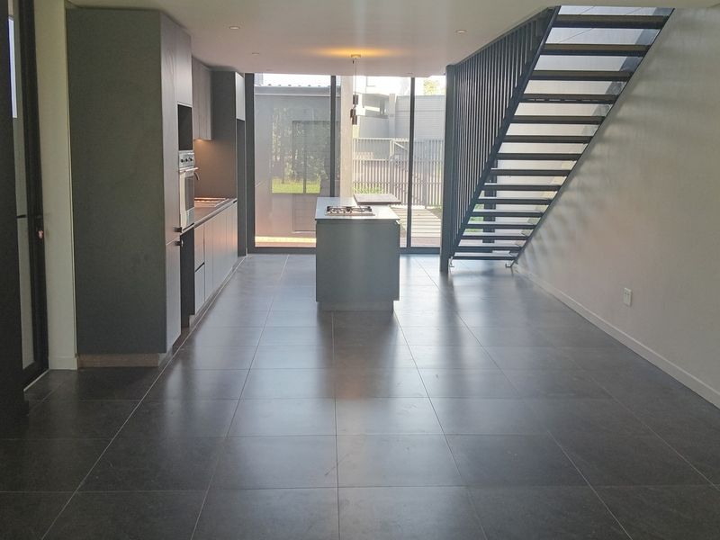 Modern open-plan kitchen and living area featuring sleek cabinetry, a central island with hob, tiled floors, and a contemporary staircase leading to the upper level.