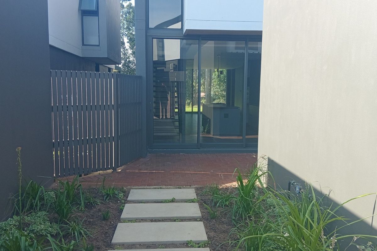 A modern townhouse rear exterior featuring a paved walkway, concrete stepping stones, and large sliding glass doors leading into the living area.