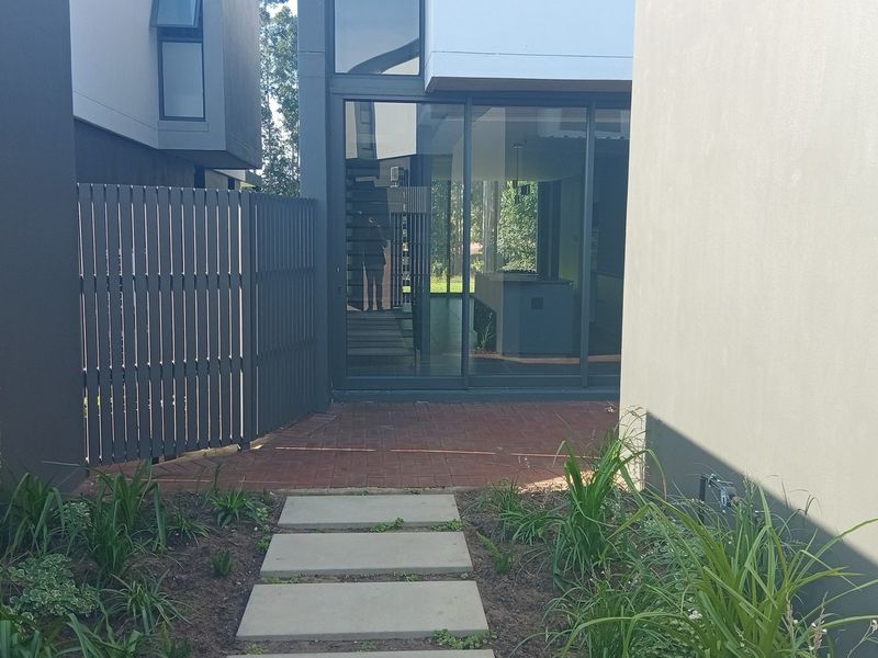 A modern townhouse rear exterior featuring a paved walkway, concrete stepping stones, and large sliding glass doors leading into the living area.