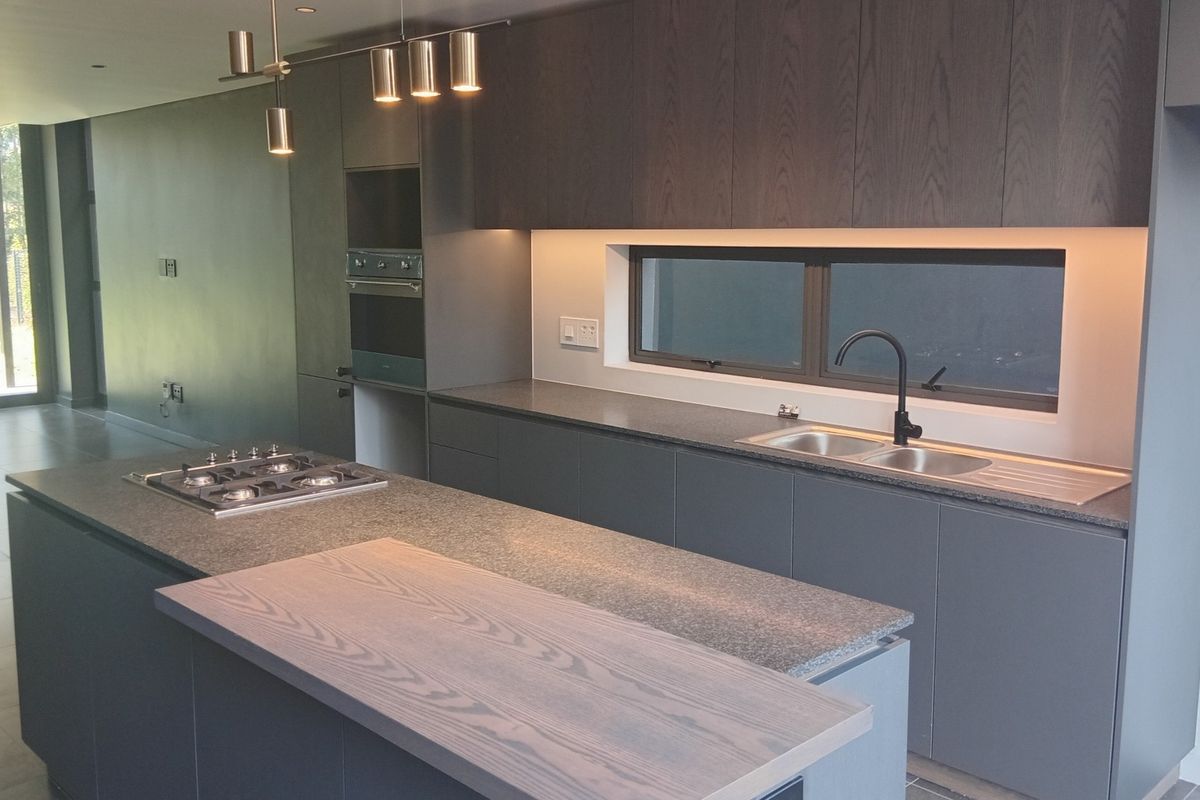Modern kitchen featuring a central island with gas hob, sleek dark cabinetry, stone countertops, integrated appliances, and recessed lighting in an open-plan layout.