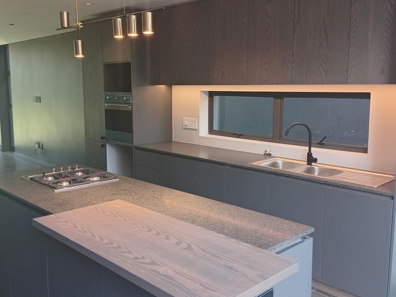 Modern kitchen featuring a central island with gas hob, sleek dark cabinetry, stone countertops, integrated appliances, and recessed lighting in an open-plan layout.